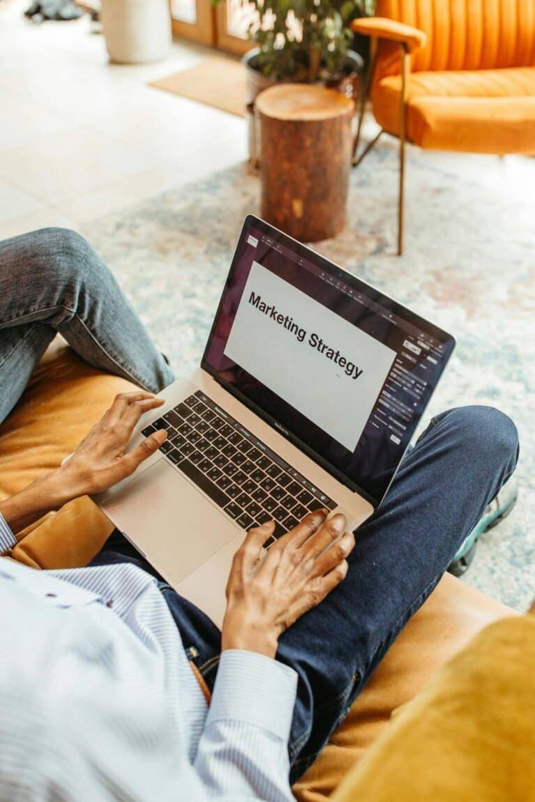 Osoba z laptopem na kolanach, na ekranie prezentacja Marketing Strategy